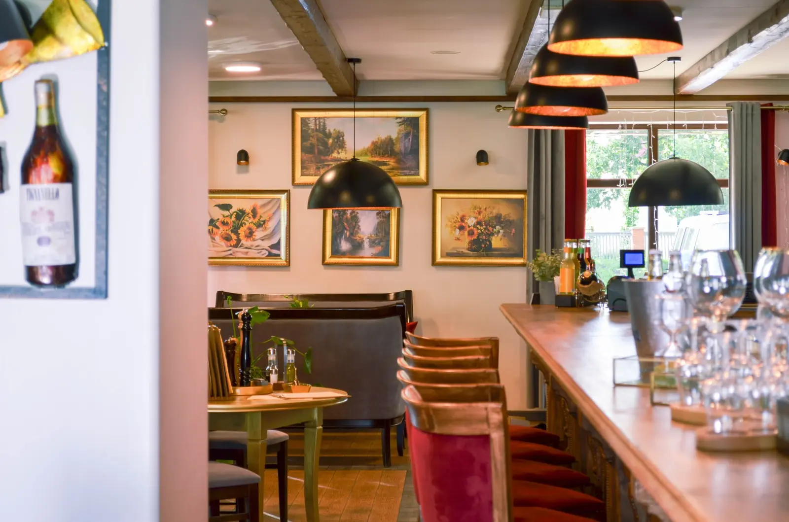 Wnętrze restauracji z drewnianym barem, obrazami i czerwonymi krzesłami